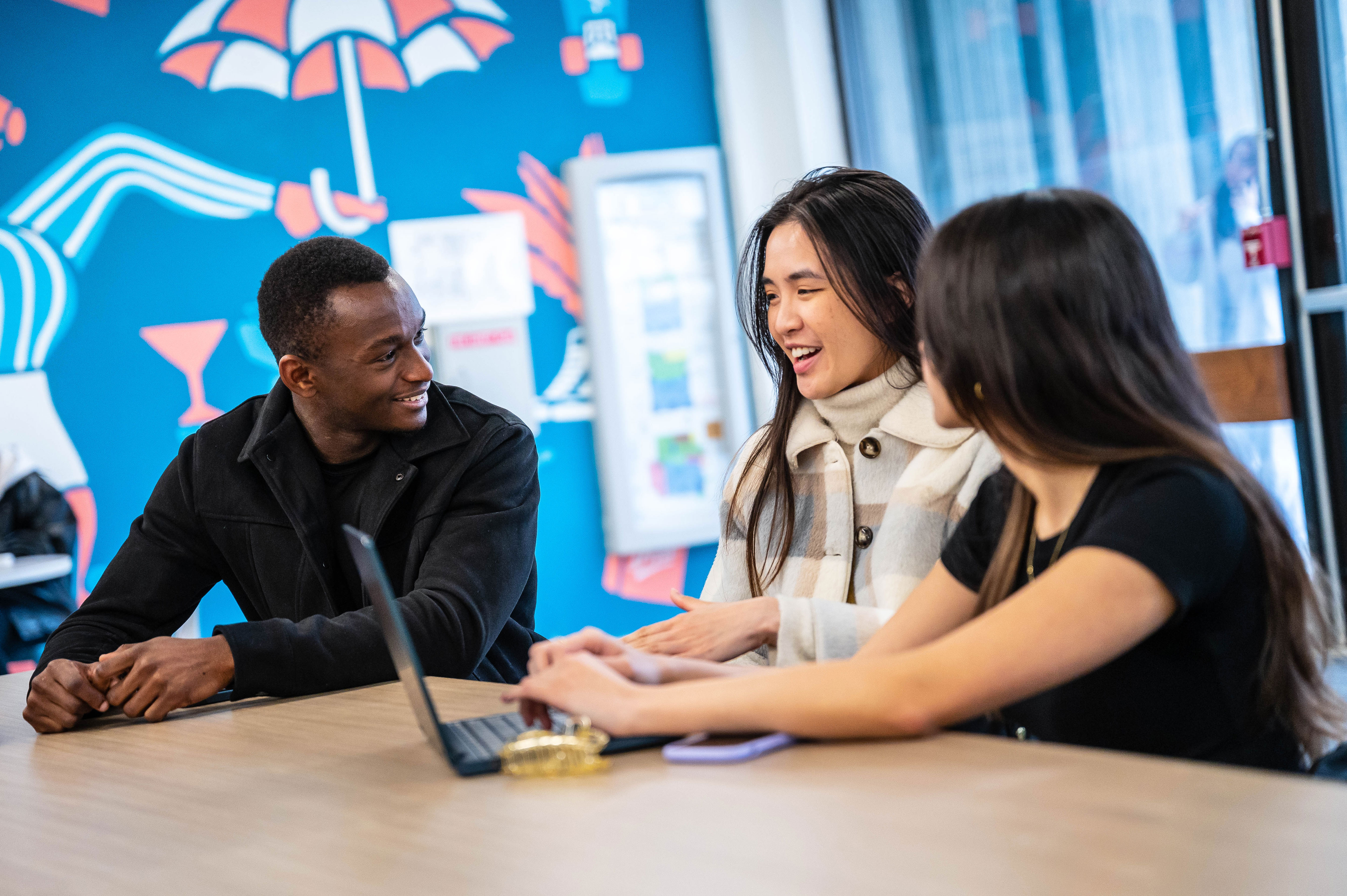 Three students sitting together and chatting at a table in the UBC Life Building