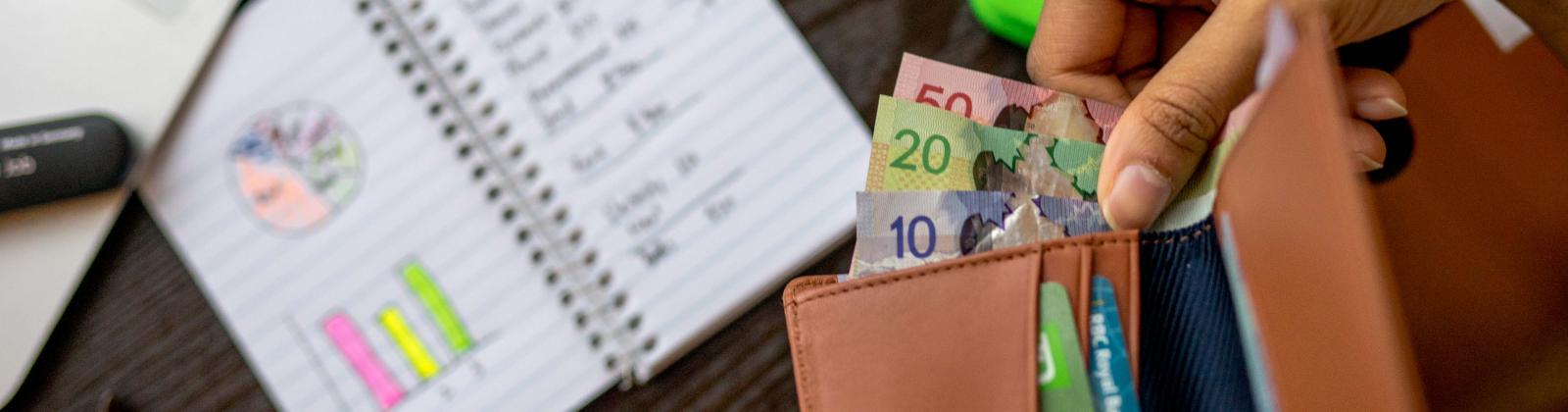 Birds-eye view shot of someone taking out cash from a wallet and of a desk with a calculator, bills, pens, and other items.