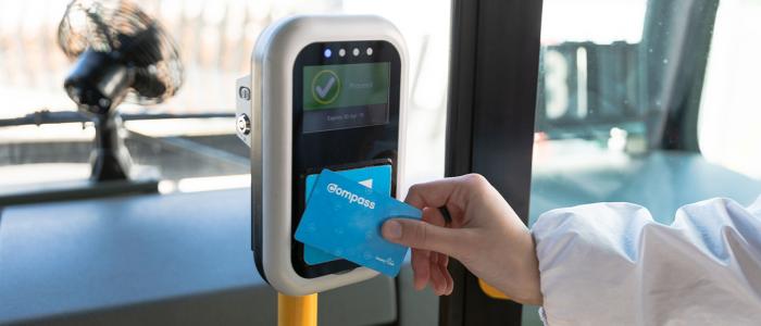 A hand tapping a Compass card against the TransLink card reader on the bus