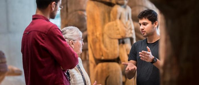 UBC student at Museum of Anthropology introducing exhibit to an elderly woman and a tall man
