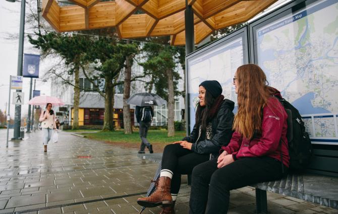 Two students waiting at the bus stop and chatting