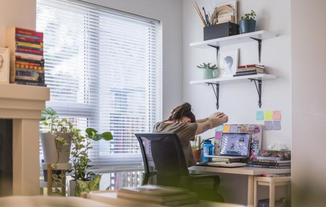 A student sitting at their work from home desk space while doing arm stretches