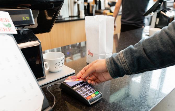 A student tapping their credit card on a payment terminal at JJ Bean Coffee Roasters