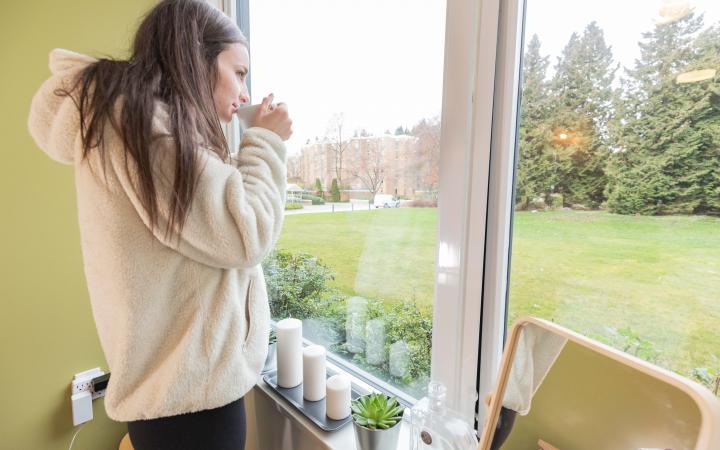 Student sipping tea looking out of a their Totem dorm room window