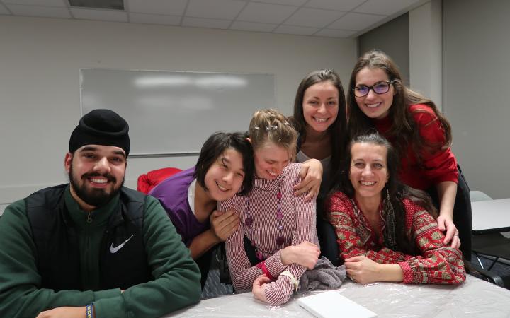 A photograph of six members of UBC Best Buddies. They are all seated or standing around a table, smiling for the photograph. 